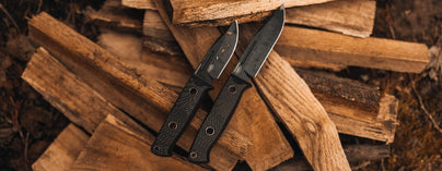 Two black camping knives with textured handles rest on split firewood, ready for rugged outdoor adventure.