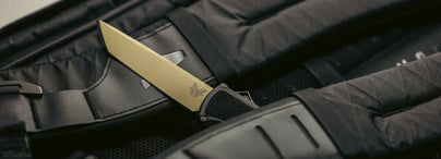 Brass folding knife resting on black tactical gear, illustrating manual and assisted opening mechanisms.
